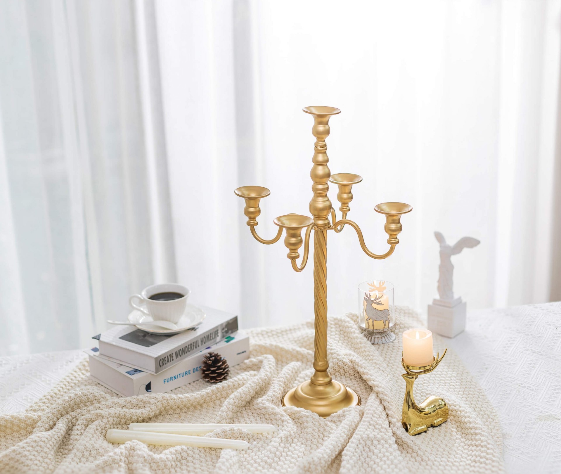 A brass candelabra styled on a soft ivory throw with coffee, books and a small deer candle holder — a Cartivou décor arrangement
