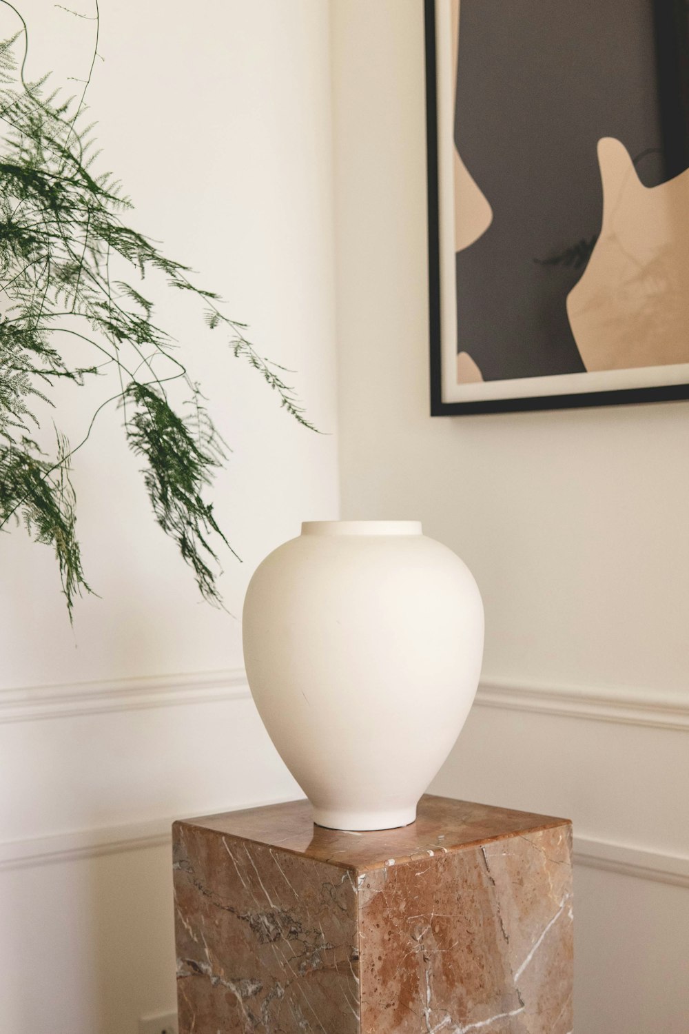 White ceramic vase styled on a stone pedestal in a warm neutral room